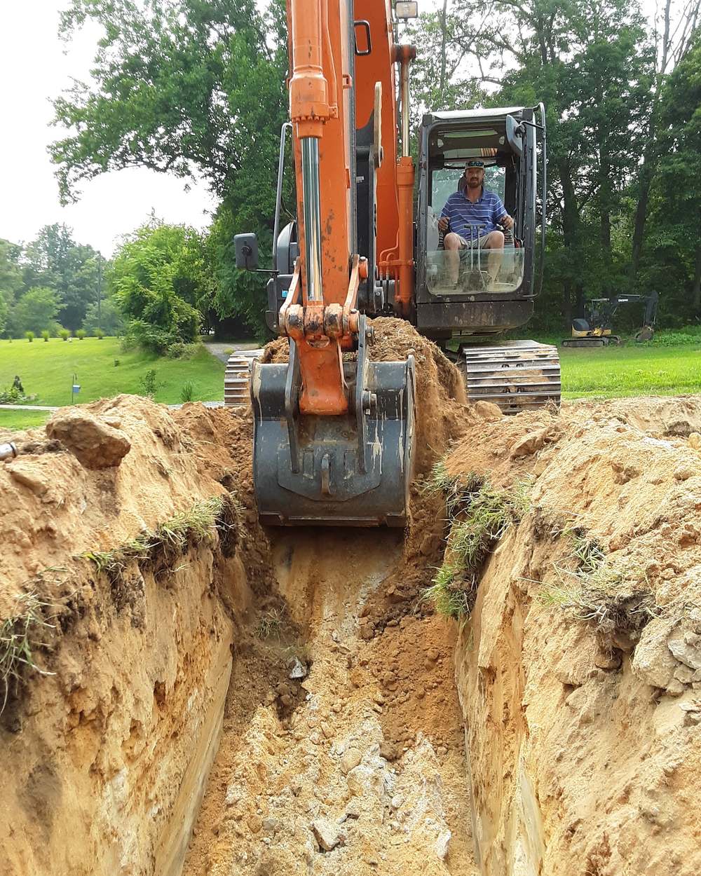 Dirt Dog Drainfields operator digging a septic trench with a tracked excavator