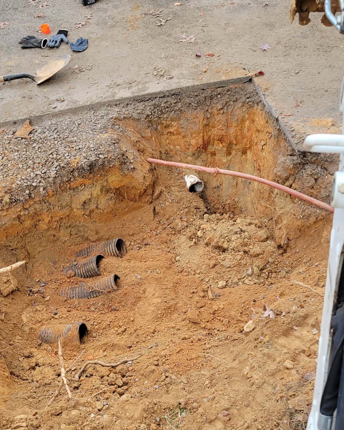 Excavated pit exposing drainfield lateral pipes during a distribution box repair