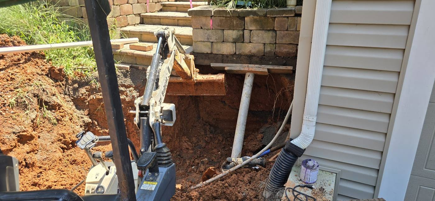 Compact excavator working beside a home's foundation during a septic system repair