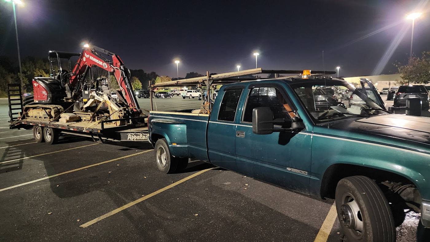 Dirt Dog Drainfields truck and trailer loaded with excavators, staged at night