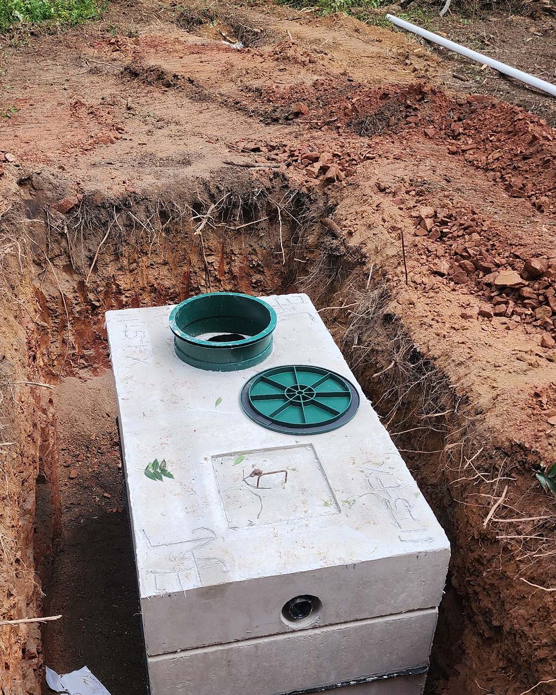 New precast concrete septic tank with green risers set in an excavated trench