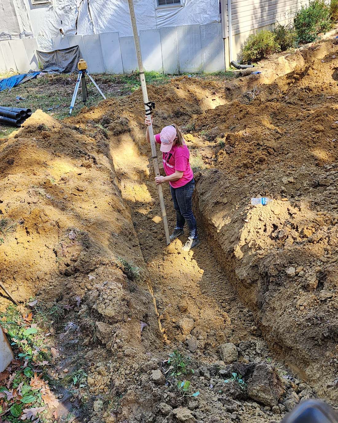 Crew member checking trench depth with a grade rod during a septic line repair